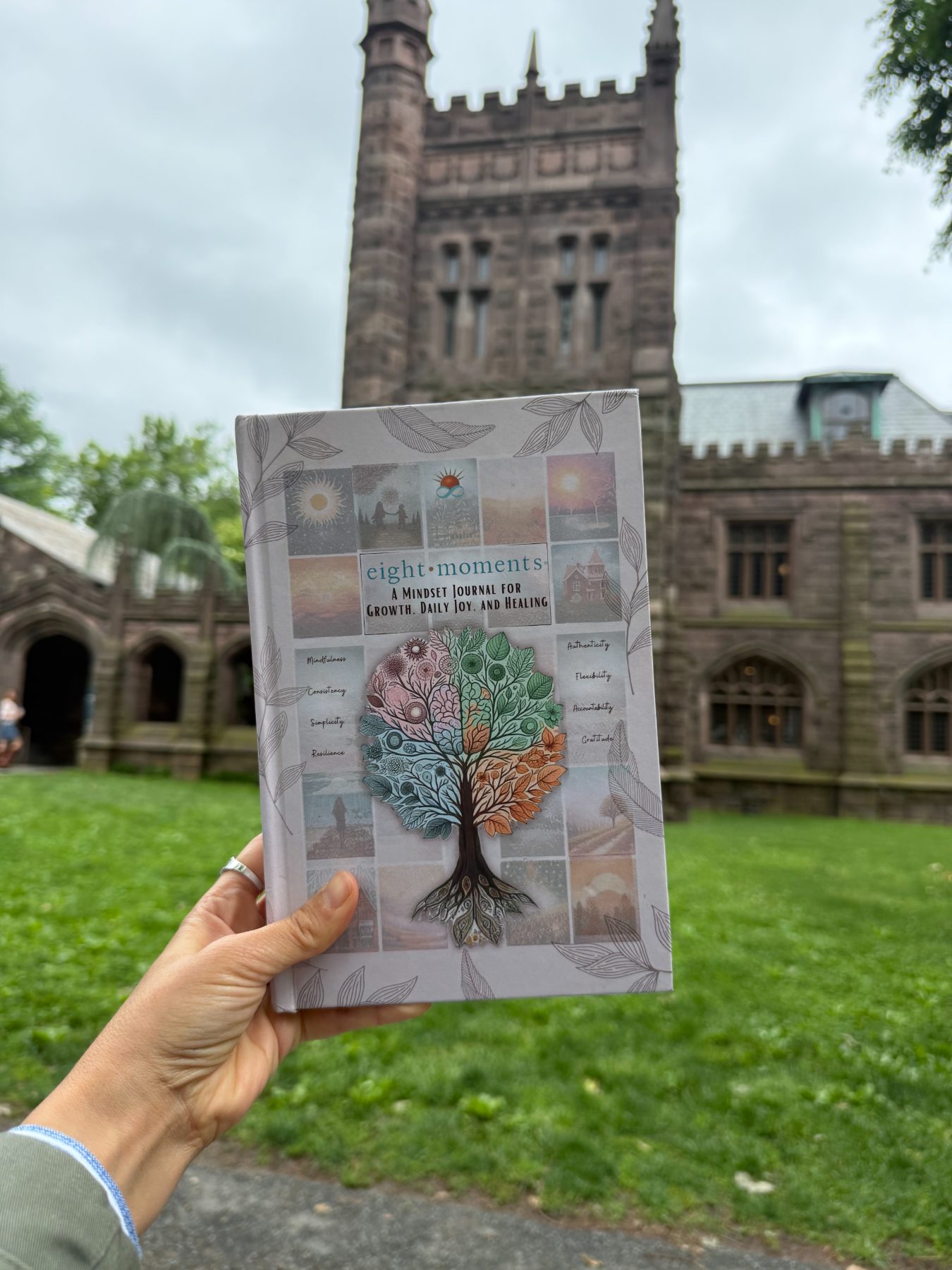 The journal held up in front of a stone university tower