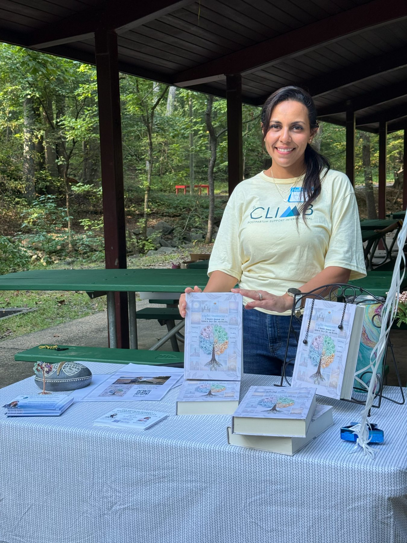 Heba displaying the journal at a community event table in the woods