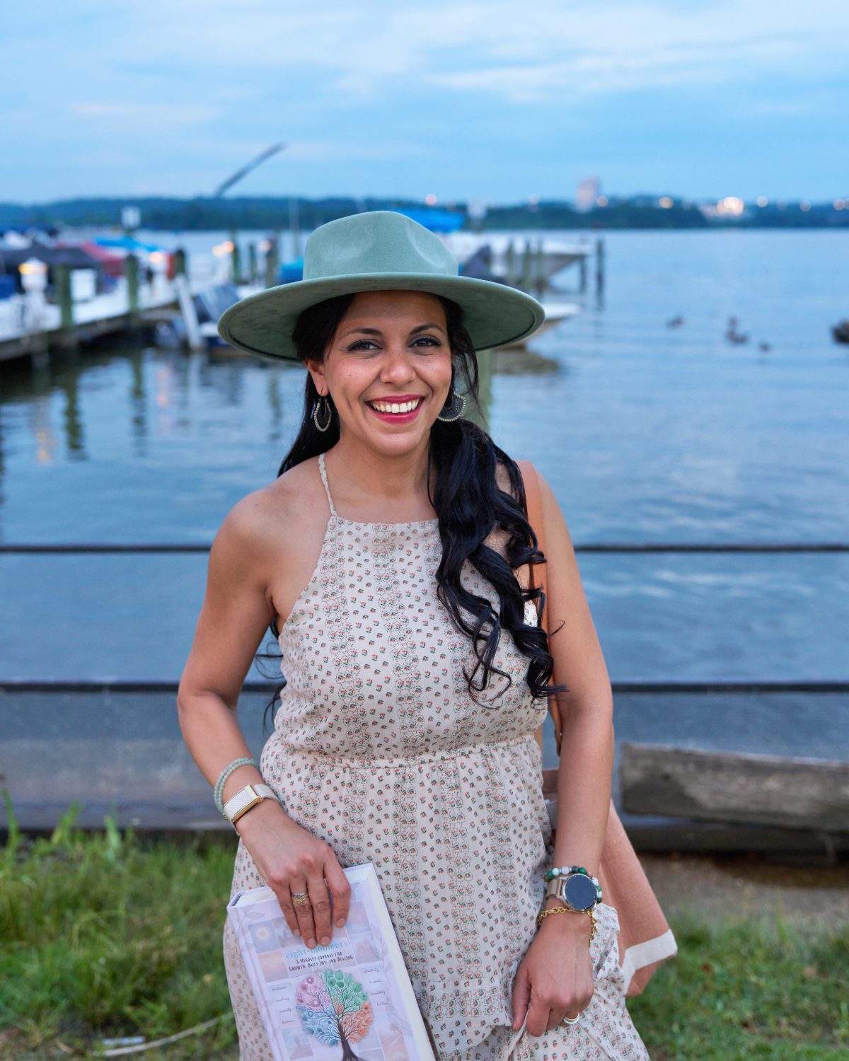 Heba Saleh smiling by the water, holding the Eight Moments journal