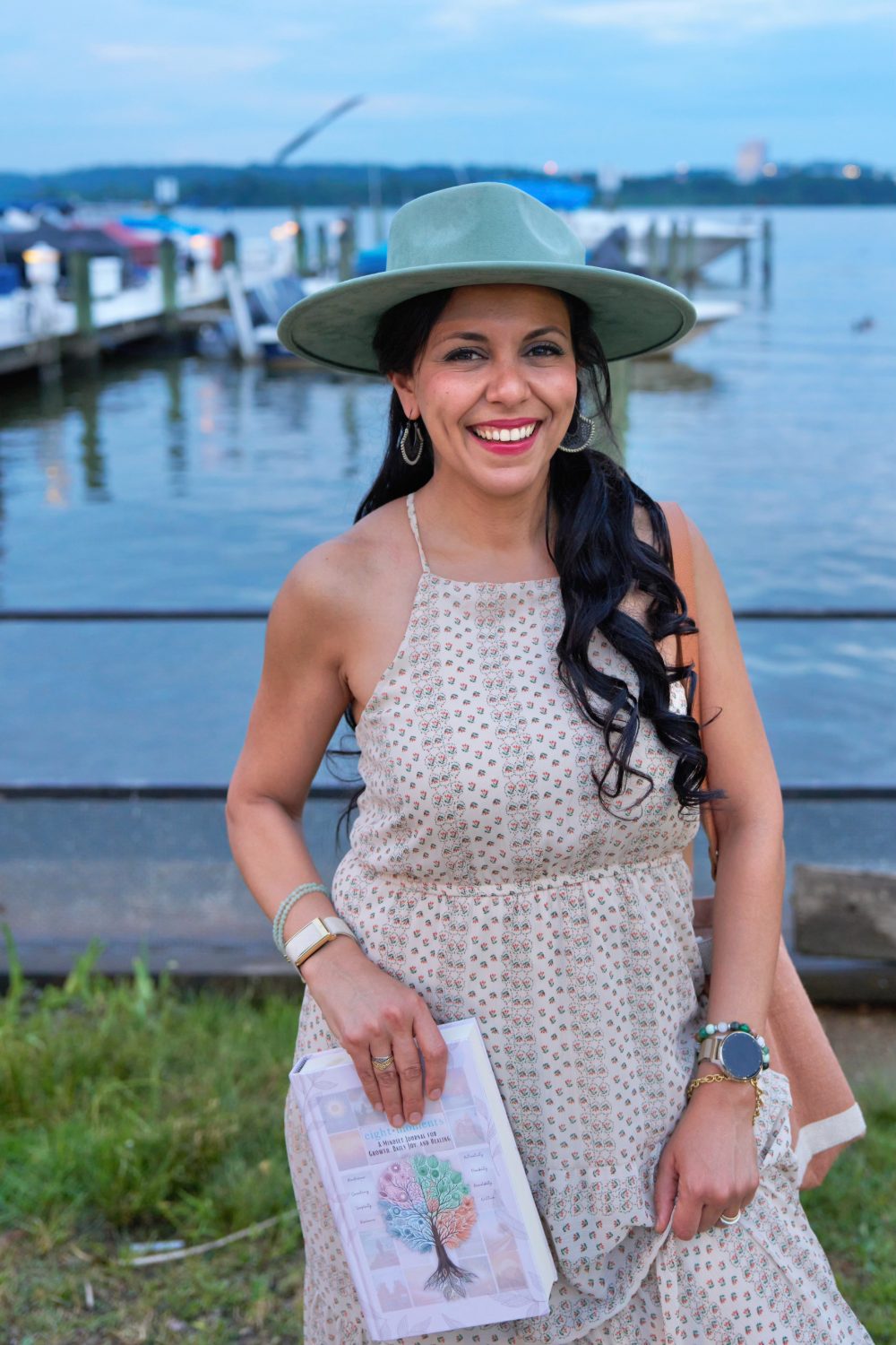 Heba, founder of Key of Life, smiling by the water holding the Eight Moments journal