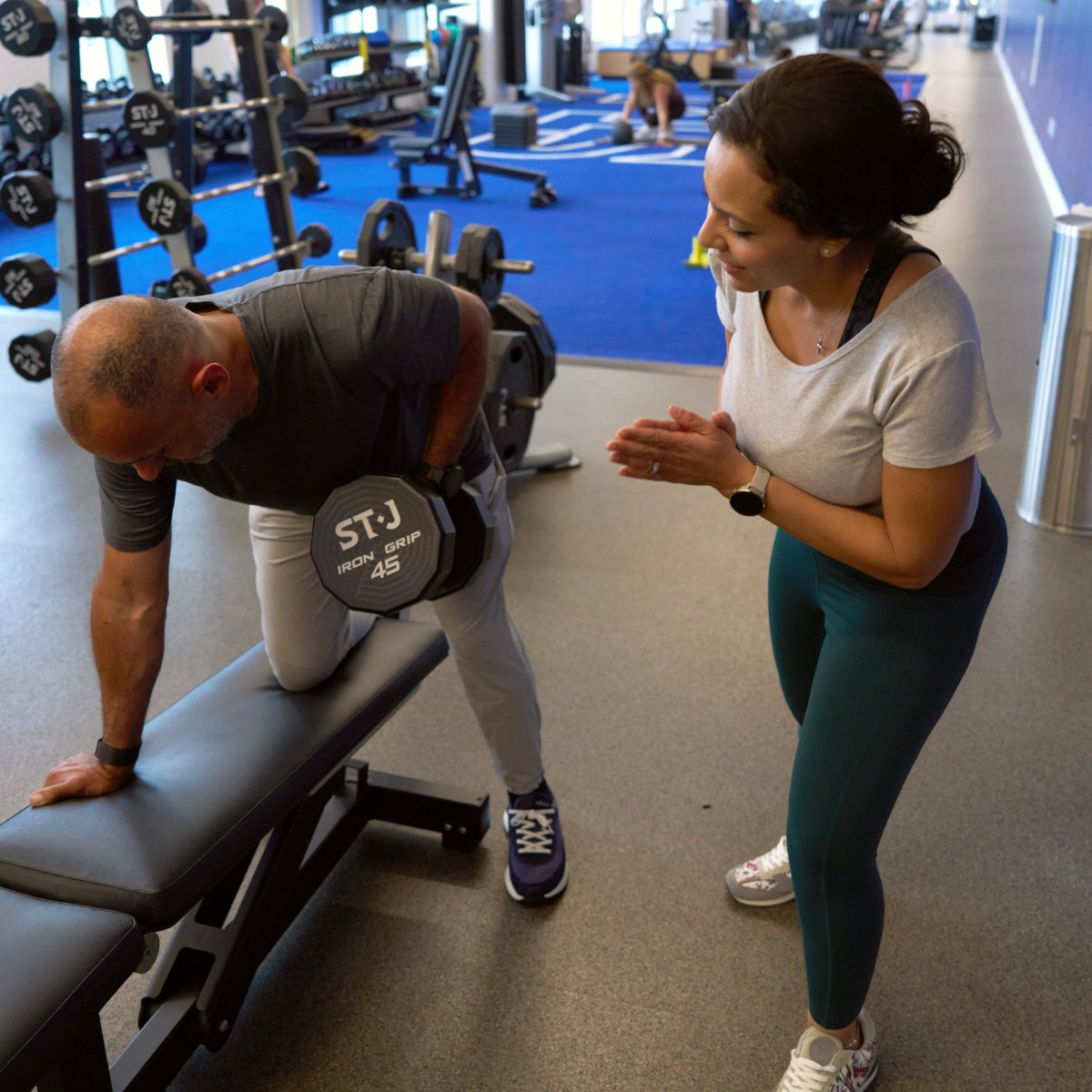 Heba coaching a client through a dumbbell row at the gym