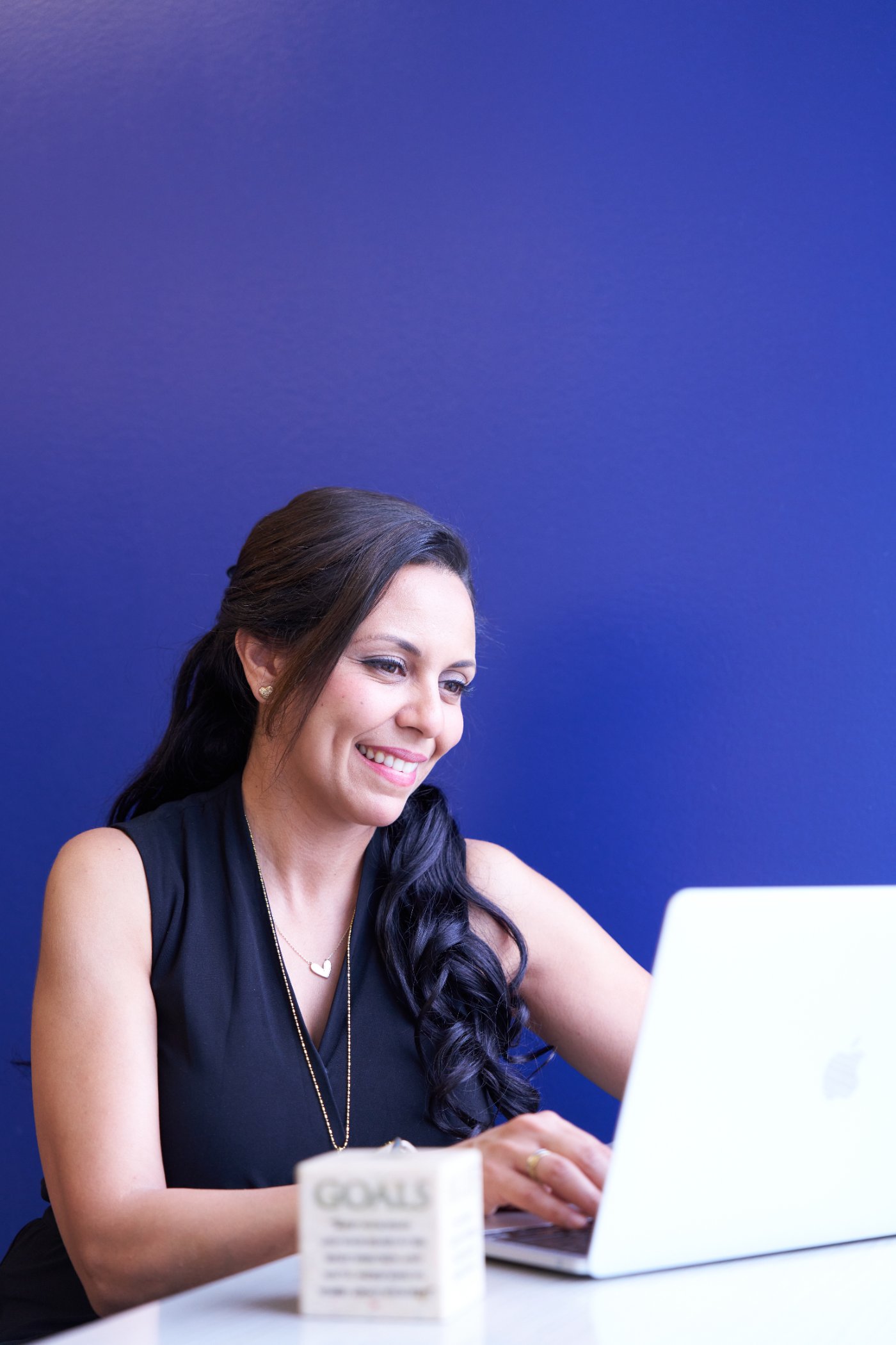 Heba smiling while joining a virtual Mindset Groups session on her laptop, with a "Goals" block beside her